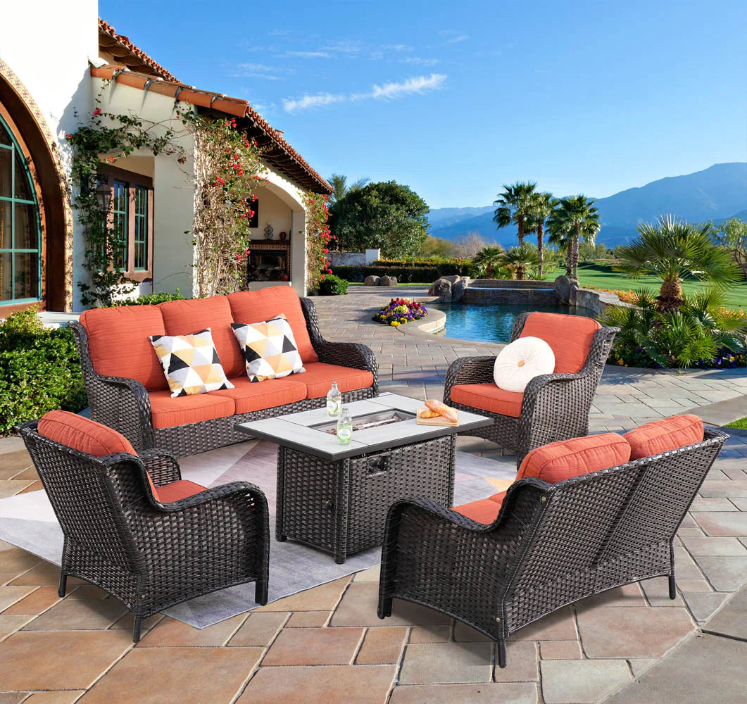 The Ovios dark wicker patio set with vibrant orange cushions and central fire pit table graces a luxurious poolside terrace