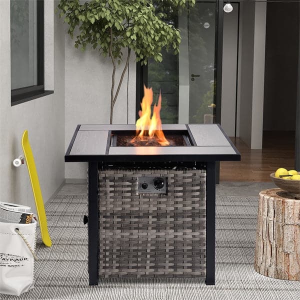 The Ovios square fire pit table burns brightly on the modern patio, surrounded by a woven base, yellow skateboard, and tree stump side table